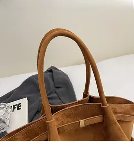 Gros plan de la poignée en daim marron du sac cabas avec coutures fines et boucles dorées