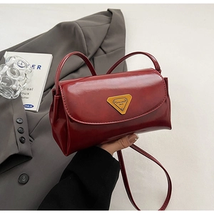 Detail view of burgundy oil wax leather pillow bag with gold triangle plaque and strap