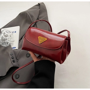 Close-up of wine red oil wax leather pillow bag with gold triangle logo and strap