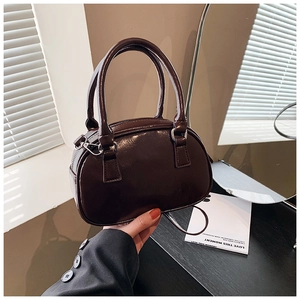 Detail view of burgundy glossy patent leather bag with dual handles and metal hardware