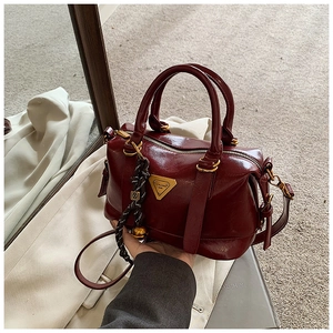 Macro detail of wine red retro handbag featuring gold logo plate and woven logo charm