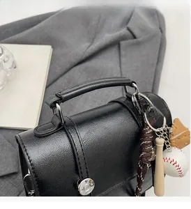 Detail of black pebbled leather handbag with cylindrical handle and baseball charm set