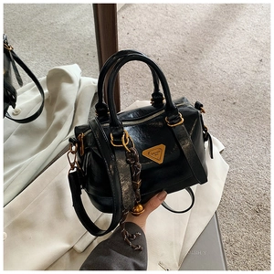 Detail of black glossy Boston bag with gold metal logo and braided rope pendant