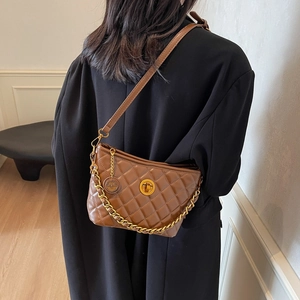 Quilted brown chain shoulder bag in retro style worn by a model in a black blazer