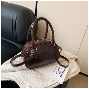 Detailed view of deep brown glossy leather bowling bag with silver hardware on a white rug