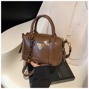Detailed close-up of brown glossy bowling bag with gold triangular logo and woven charm