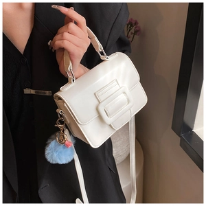 Dettaglio di una borsa a patta bianca con fibbia decorativa e ciondolo a pompon blu