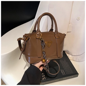 Detail of dark brown glossy Boston bag with metal logo and woven knot accessory