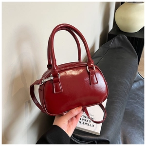 Detail of burgundy glossy leather handbag with dual handles and silver hardware clips