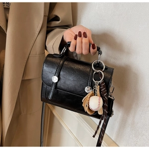 Close-up of black retro handbag with dual silver buckles and baseball glove pendant charms
