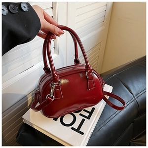 Glossy red patent leather bowling bag with silver hardware on a luxury leather sofa