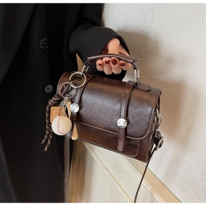 Close-up of brown textured leather mini bag with baseball charm and metallic buckle details