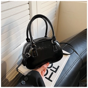 Detail of a mini black patent leather bowling bag with twin handles and top zipper
