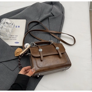 Detail of a brown vintage square bag with baseball charm on a gray blazer background