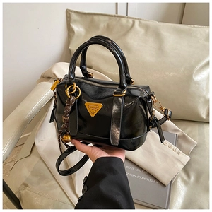 Close-up of black glossy patent leather Boston bag featuring golden metal triangle hardware