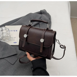 Detail of dark brown leather crossbody bag featuring metal buckle and vintage handle