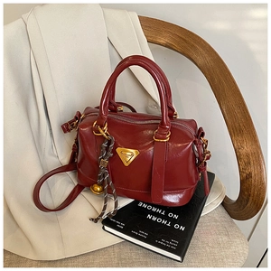Detail of burgundy Boston bag with gold hardware and charm on a black book