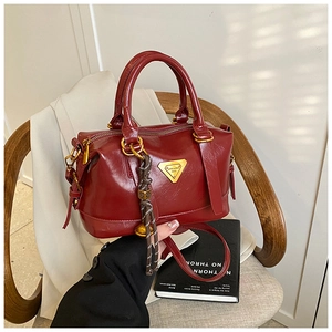 Detail of dark red Boston bag with polished finish and iconic triangle metal logo