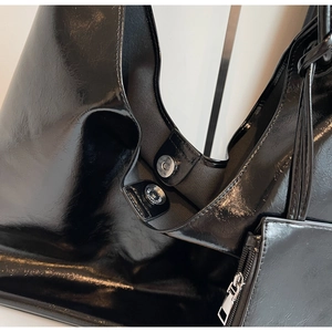 Detail of glossy black shoulder bag featuring metal magnetic clasp and smooth texture