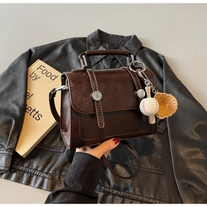 Detail of dark brown polished handbag with baseball charms and silver ring buckle