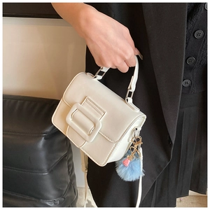 Dettaglio borsa bianca in pelle con fibbia quadrata e ciondolo con pompon in pelliccia blu