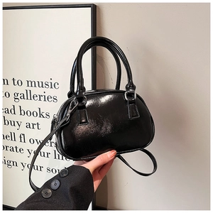 Detailed view of a mini black patent leather bowling bag held in hand with slim strap