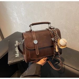 Detail of a brown leather crossbody bag with metal buckle and baseball charm
