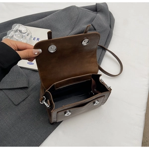 Detail view of the magnetic metal clasp and dark interior zipper pocket of the brown bag