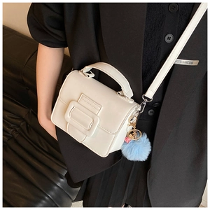 Dettaglio di una borsa a tracolla in pelle bianca con manico e pompon azzurro