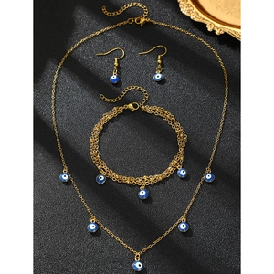 Macro shot of gold Evil Eye necklace, bracelet and earrings set on dark textured surface