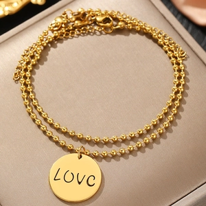 Makro-Detail von goldenem zweischichtigem Perlenarmband mit LOVE-Gravur-Anhänger