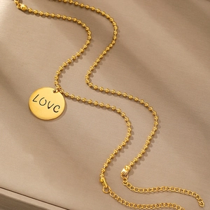 Goldenes Armband mit rundem LOVE-Anhänger und Kugelkette auf Lederhintergrund