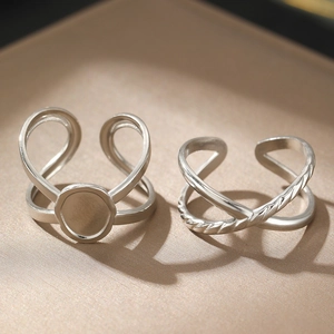 Close-up of silver open rings featuring a round disc and cross X design on a beige tray