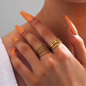 Close-up of stacked gold stainless steel layered rings on model with elegant orange nails