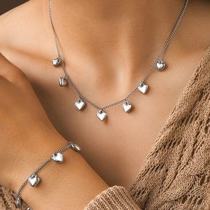 Detailopname van hartjes ketting en armband set gedragen op een bruine gebreide trui