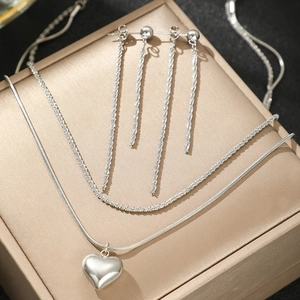 Détail du collier avec pendentif cœur argenté et boucles d'oreilles à pompons longs