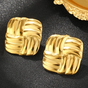 Macro shot of square gold earrings with textured woven pattern on a black leather background