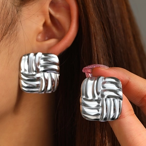 Detailed view of silver square stud earrings with woven texture on a model's ear
