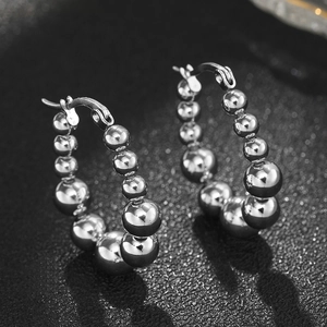 Vue macro de créoles perlées en argent poli avec perles en métal dégradé sur sable noir