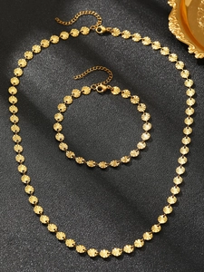 Detailed macro view of gold embossed round disc necklace and bracelet set on black background