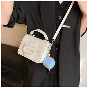 Dettaglio di una mini borsa bianca a patta con maxi fibbia e ciondolo a pompon blu chiaro