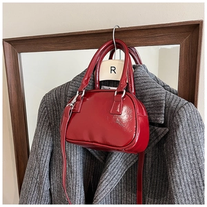 Detail view of red patent leather bowling bag with silver hardware on a grey coat
