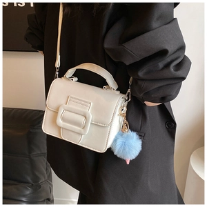 Dettaglio di una mini borsa a mano bianca con fibbia dorata e ciondolo a pompon blu