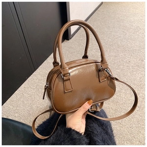 Detail of a brown glossy Boston bag featuring dual handles and adjustable shoulder strap