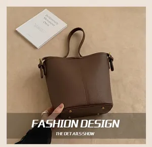 Détail d'un sac seau en cuir marron montrant la sangle réglable et les pieds en métal