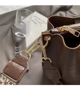Detail of dark brown leather handbag with gold hardware and colorful woven shoulder strap