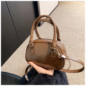 Detail view of brown leather dome bag featuring dual handles and adjustable shoulder strap