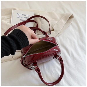 Detail of burgundy glossy faux leather bowling bag showing silver zipper and handles