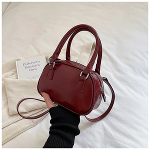 Close-up of wine red glossy mini bowling bag with dual handles and slim shoulder strap