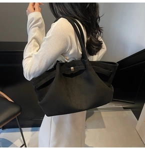 Détail d'un grand cabas en daim noir avec boucle argentée porté à l'épaule par un mannequin